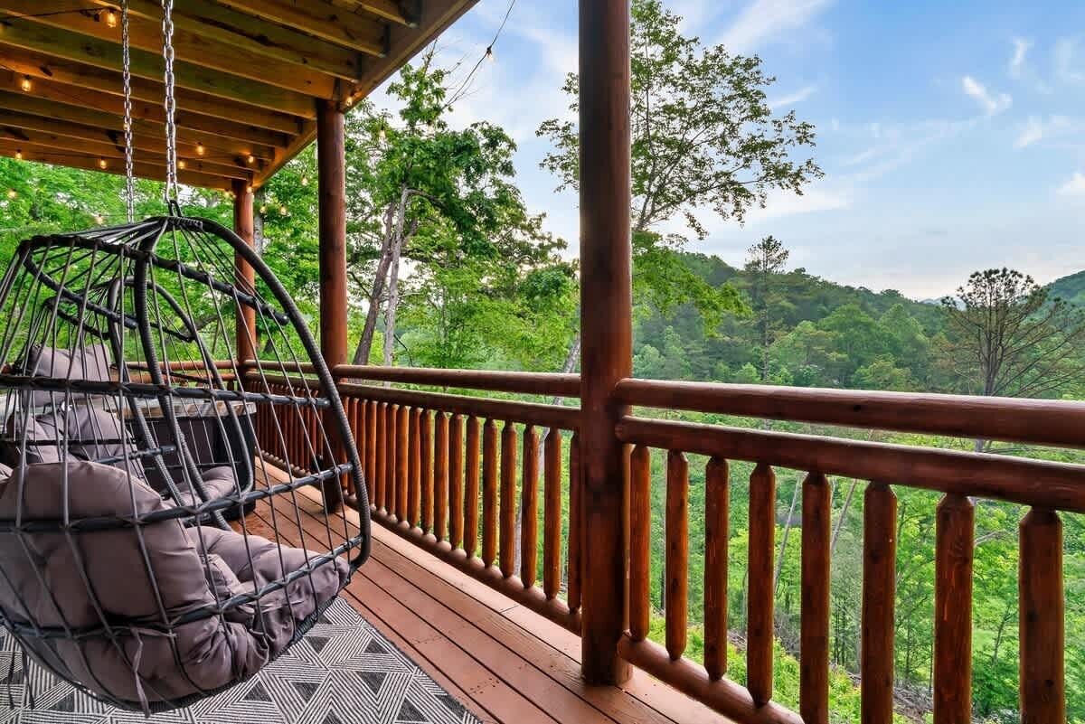 A wooden deck with a hanging chair and a view of a forested hillside.