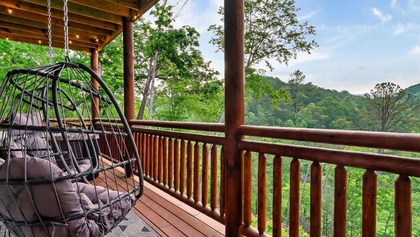 A wooden deck with a hanging chair and a view of a forested hillside. - 8-Bedroom Cabin with Indoor Pool, Private Mini Golf & Hot Tub Near Gatlinburg (Sevierville)