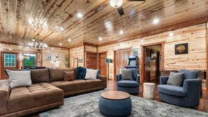 A cozy living room with a wooden ceiling, a brown sofa, blue armchairs, and a round coffee table. - 8-Bedroom Cabin with Indoor Pool, Private Mini Golf & Hot Tub Near Gatlinburg (Sevierville)