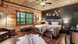 A log cabin bedroom with a bed, bench, and a large window. - 8-Bedroom Cabin with Indoor Pool, Private Mini Golf & Hot Tub Near Gatlinburg (Sevierville)