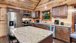 A kitchen with wooden walls, granite countertops, stainless steel appliances, and a window with a view. - 8-Bedroom Cabin with Indoor Pool, Private Mini Golf & Hot Tub Near Gatlinburg (Sevierville)