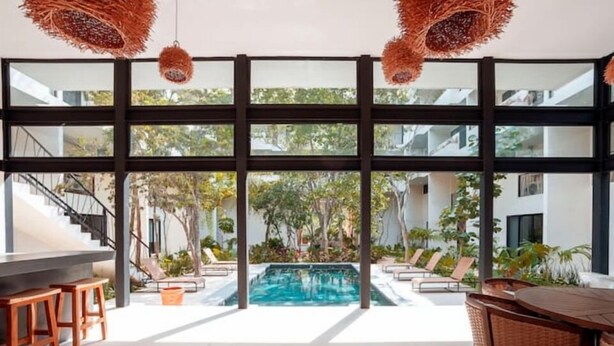Un área de piscina interior moderna con vistas despejadas, rodeada de sillones de descanso y una zona de bar con taburetes.