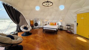 Una carpa amplia con una cama, dos lámparas, una silla y una puerta amarilla.