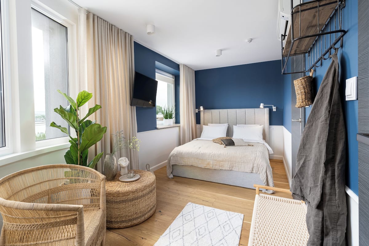 A modern bedroom with a bed, a chair, a small table, and a large window.