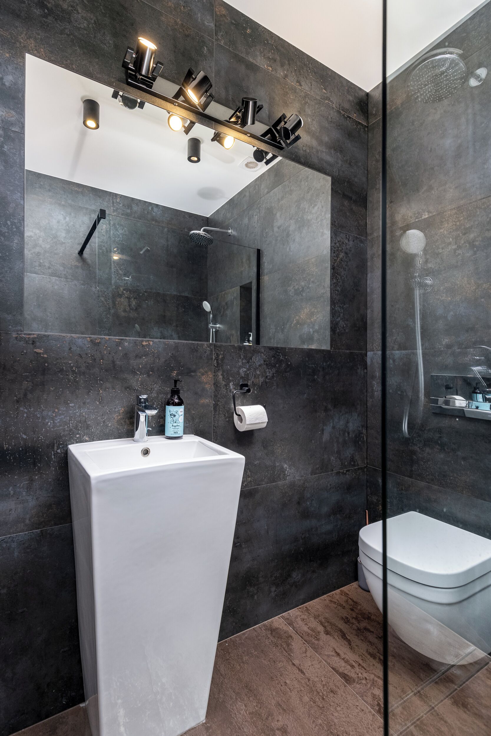 A modern bathroom with a large mirror, a white sink, and a glass-enclosed shower.