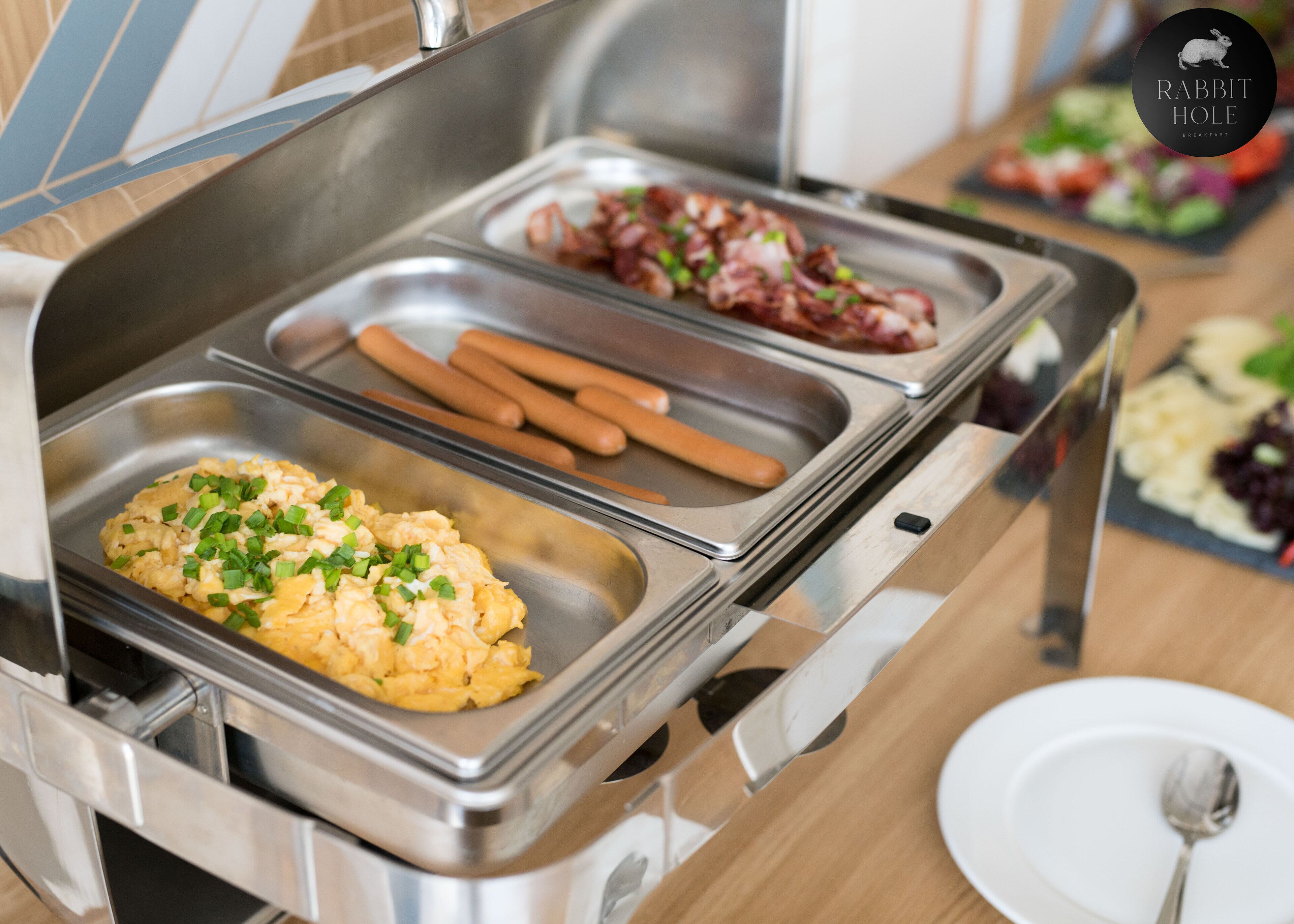A buffet with scrambled eggs, hot dogs, and a salad.