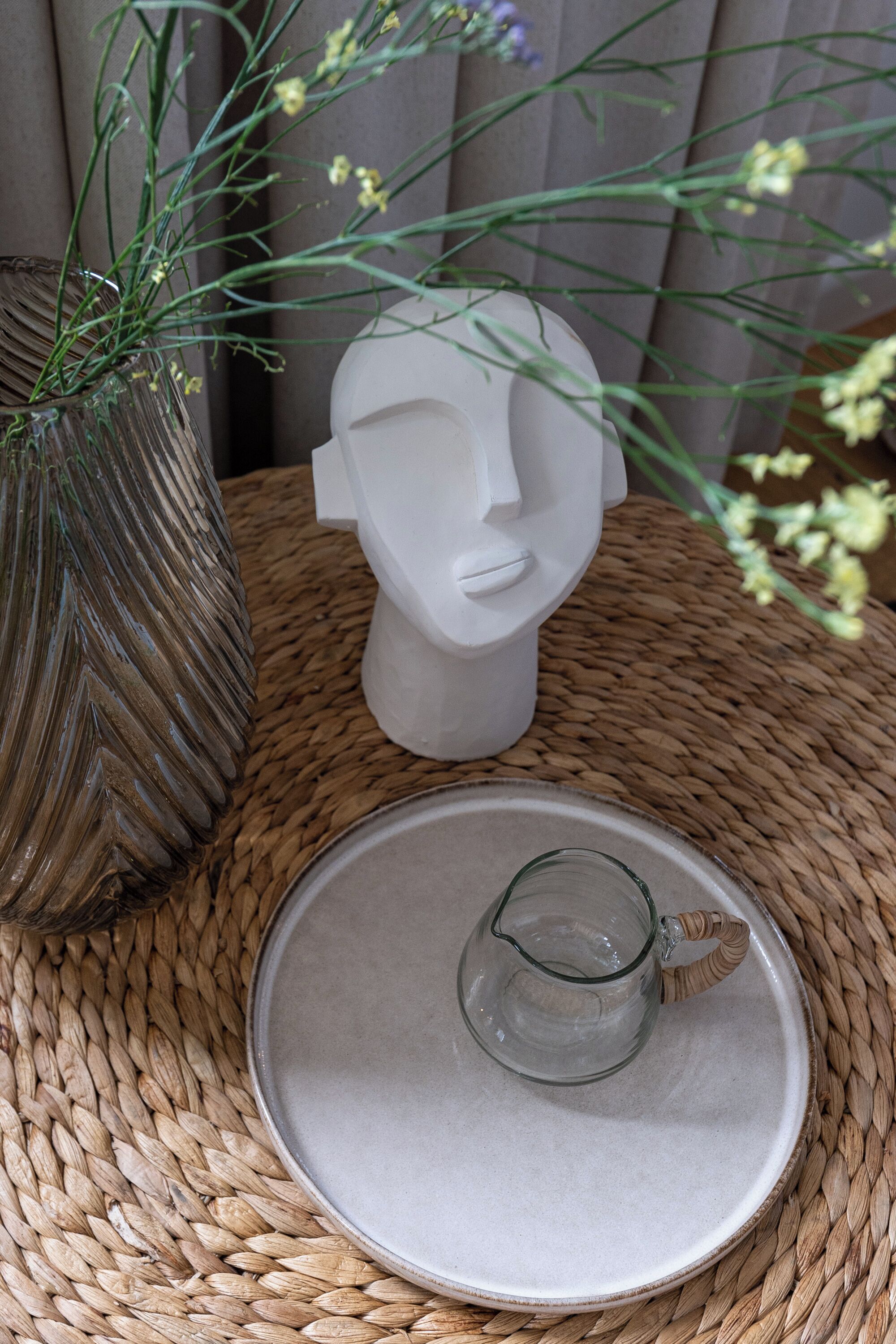 Uma mesa de fibra natural com um jarro de cerâmica e um vaso com flores.