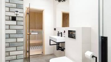 Un bagno moderno con box doccia in vetro, un water bianco, un lavandino con rubinetto nero e una porta in legno che dà accesso alla zona doccia.