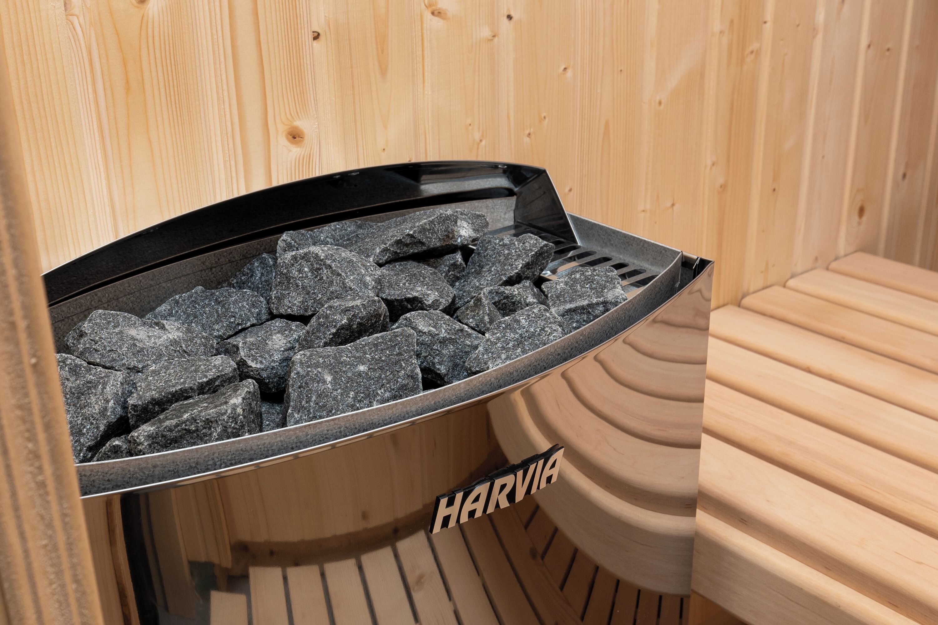 Una sauna con il marchio "HARVIA" visibile sul pavimento, interni in legno e una griglia piena di pietre.