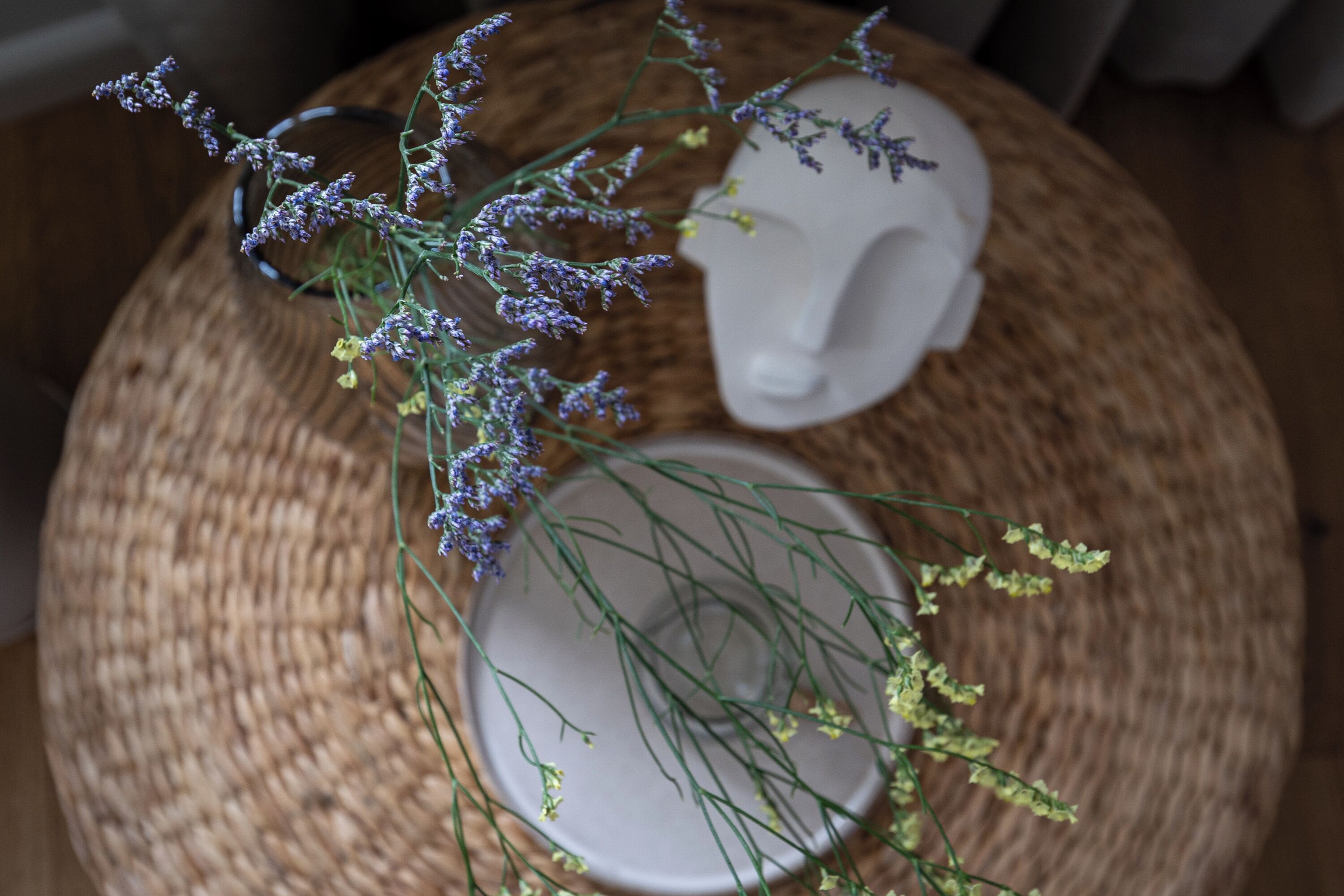A round woven table with a white ceramic vase and a white ceramic sculpture.