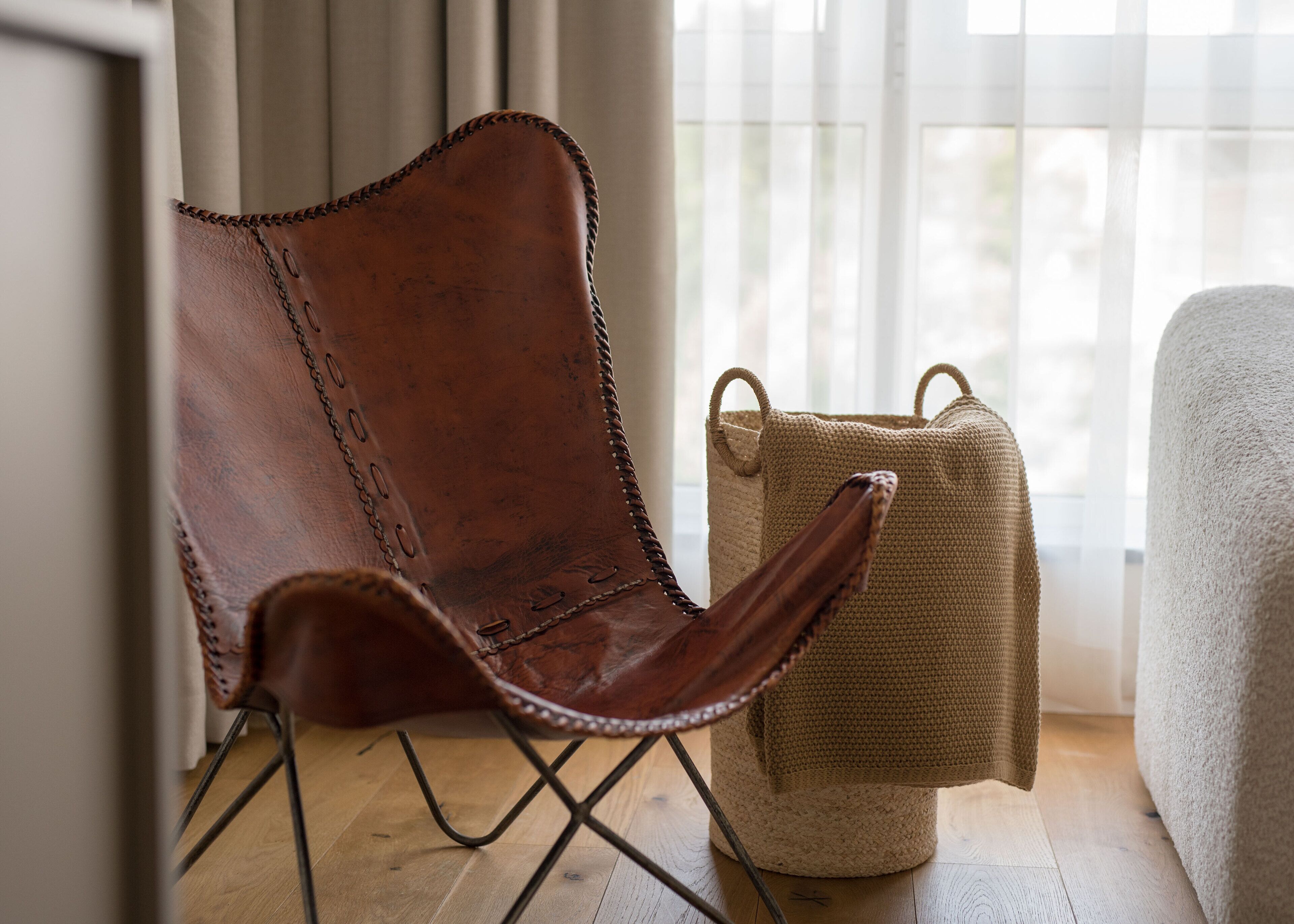A brown leather chair with metal legs, a woven basket, and a white upholstered armchair.