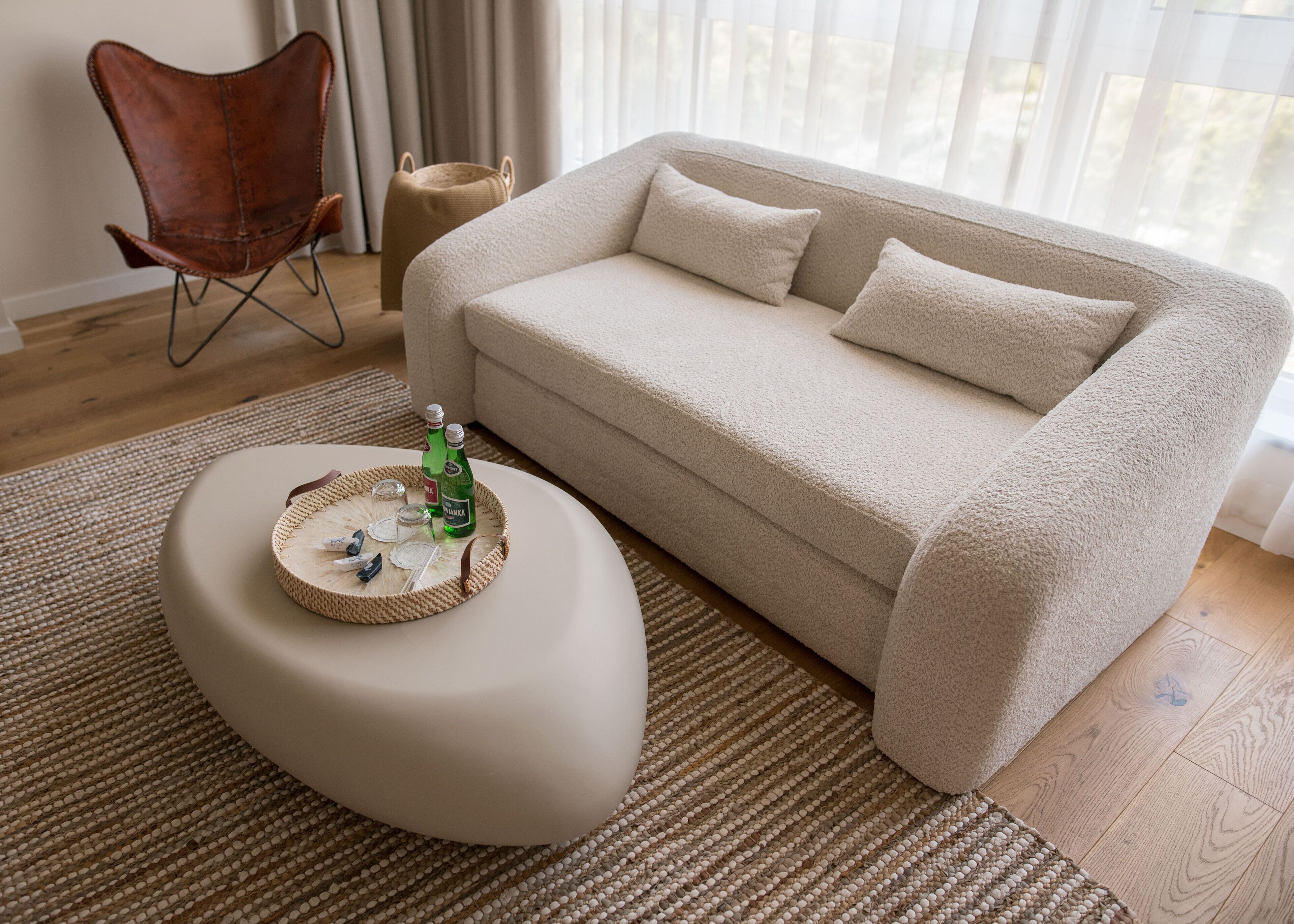 A living room with a beige sofa, a round ottoman with a woven tray, and a brown leather chair.