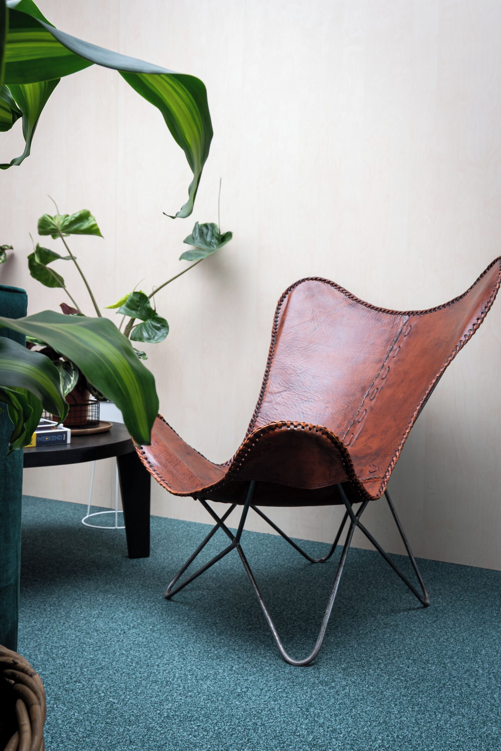A chair with a unique design, a small table with a book, and a potted plant.