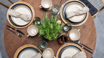 A round wooden table set for four with plates, cutlery, glasses, and a central plant.