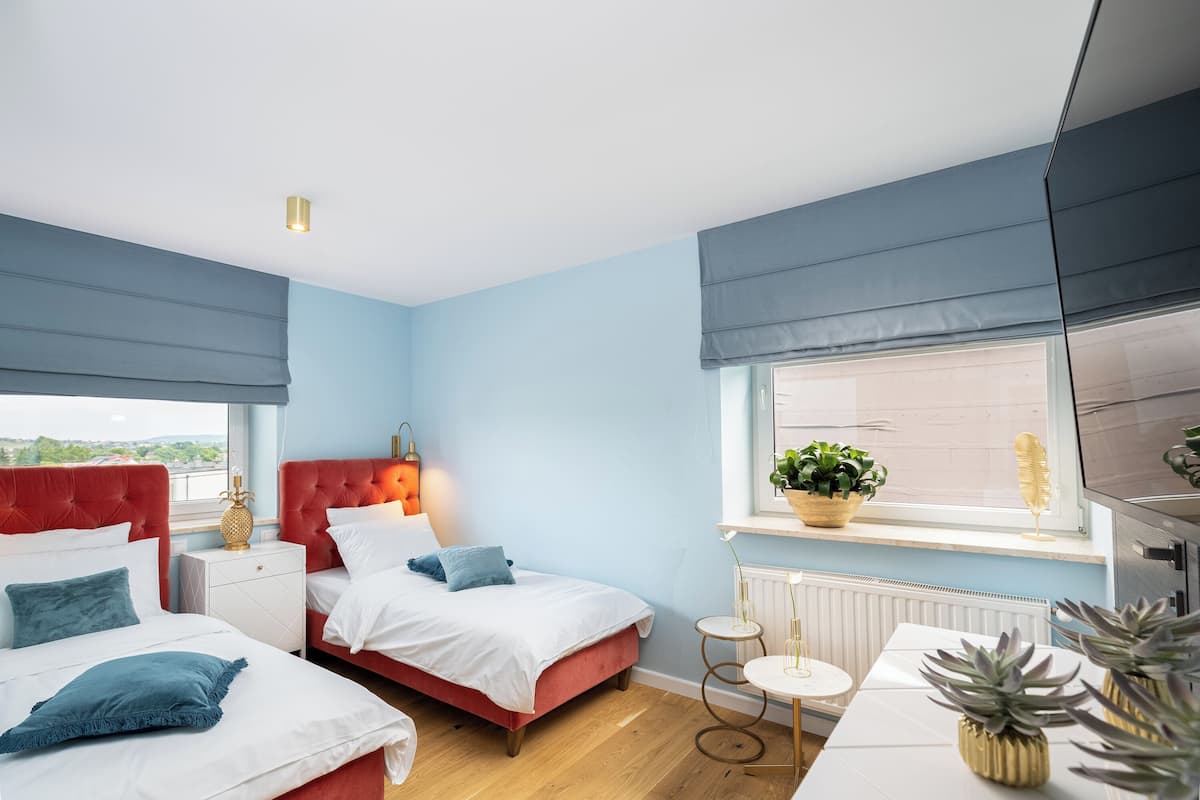 A modern bedroom with two beds, a window with a view, and a small table with plants.