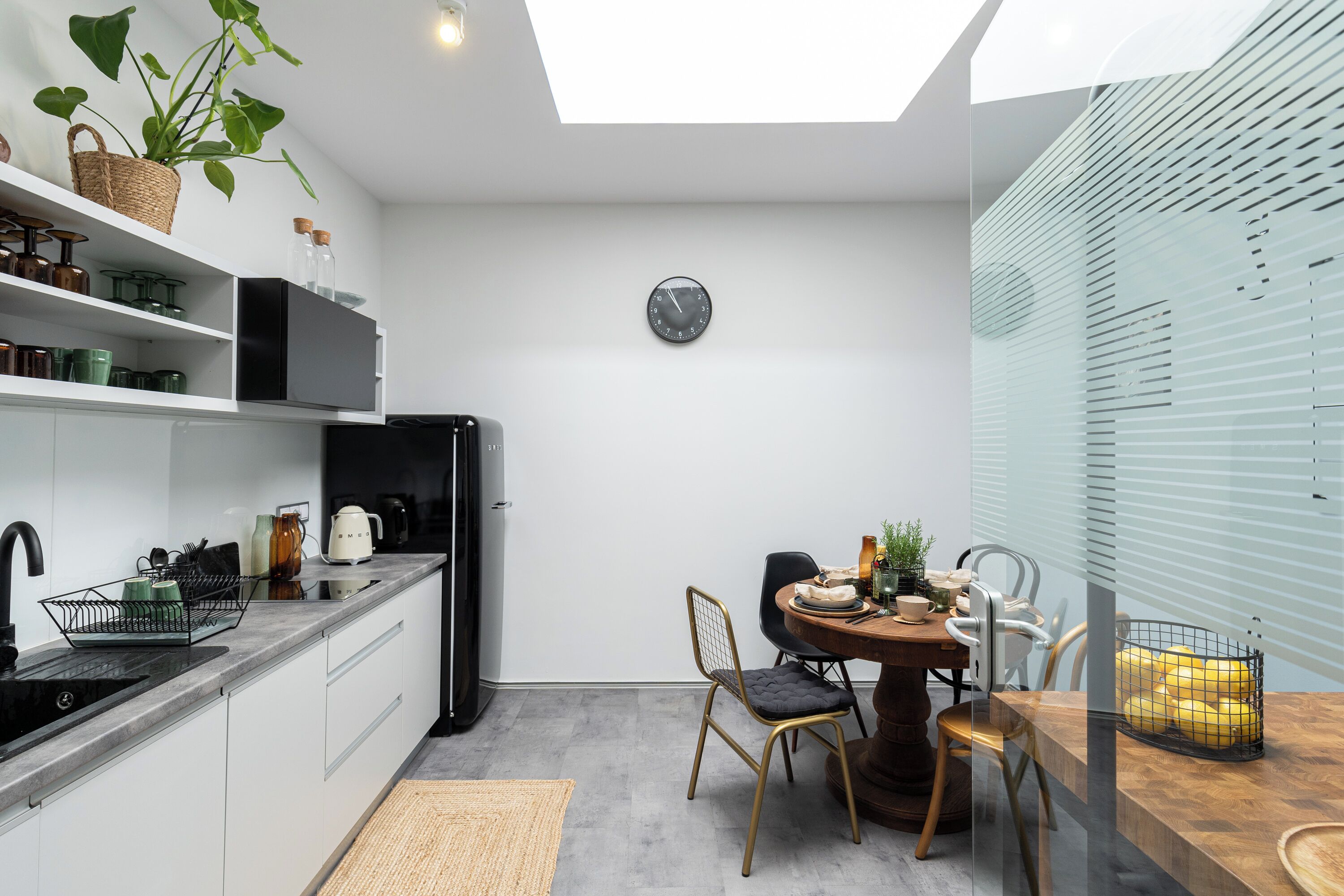 A modern kitchen with white cabinetry, a black refrigerator, and a dining area with a wooden table and chairs.