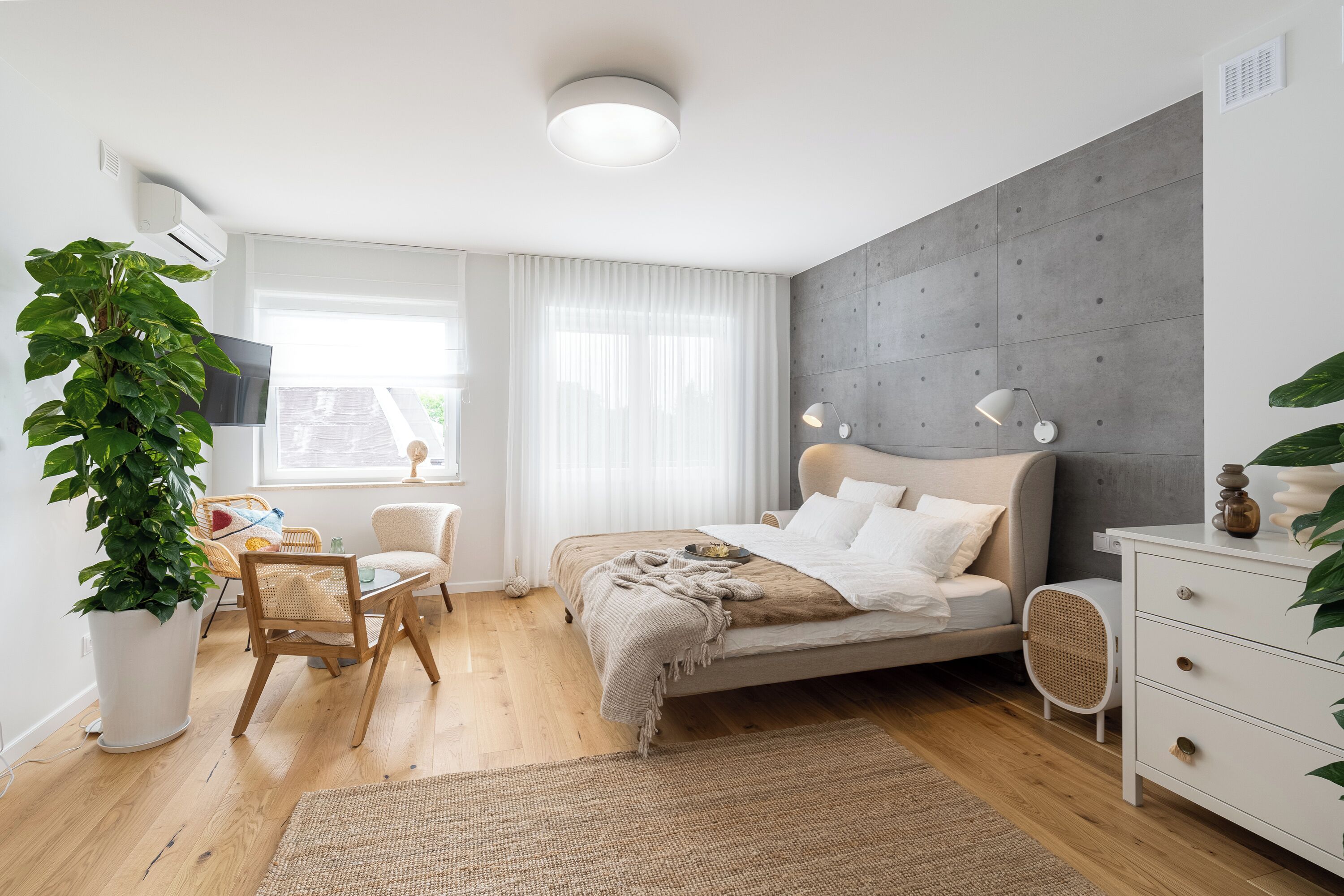 Un dormitorio moderno con cama, mesitas de noche, escritorio y una gran planta en maceta.