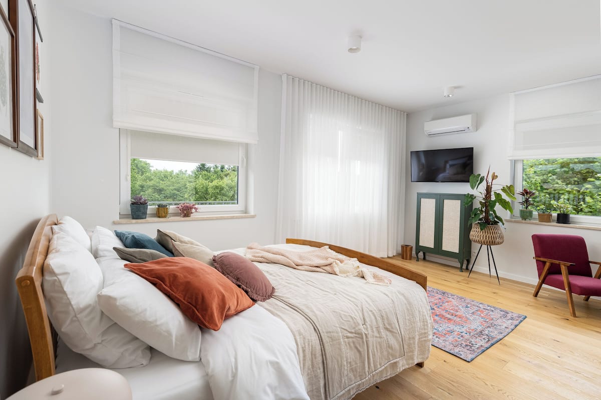 A bedroom with a bed, a red chair, a TV, and a window with blinds.