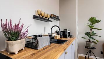 A kitchen with a wooden countertop, a sink, a coffee machine, and a potted plant.