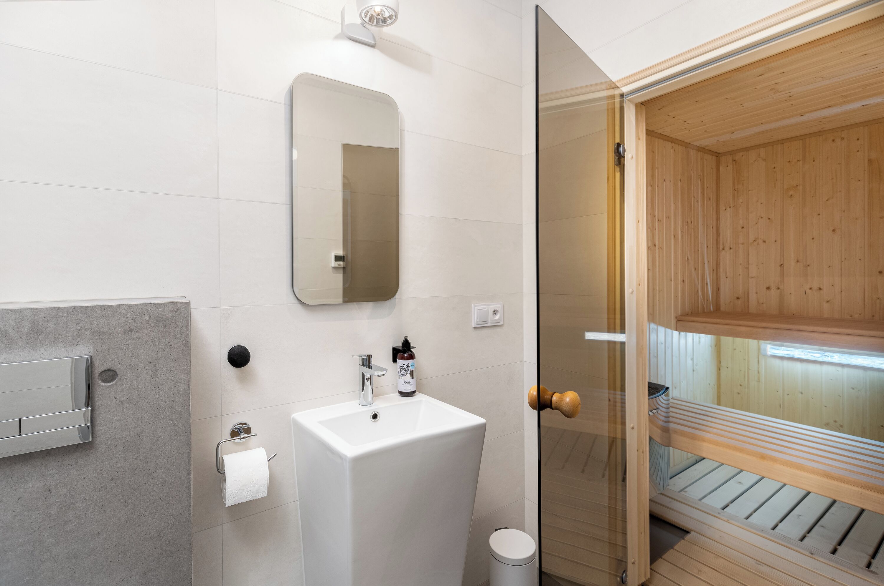 A modern bathroom with a white sink, mirror, and towel dispenser.