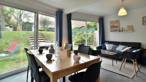 Un vaste espace de vie comprenant une grande table à manger, un canapé et une vue sur le jardin grâce à de grandes fenêtres.