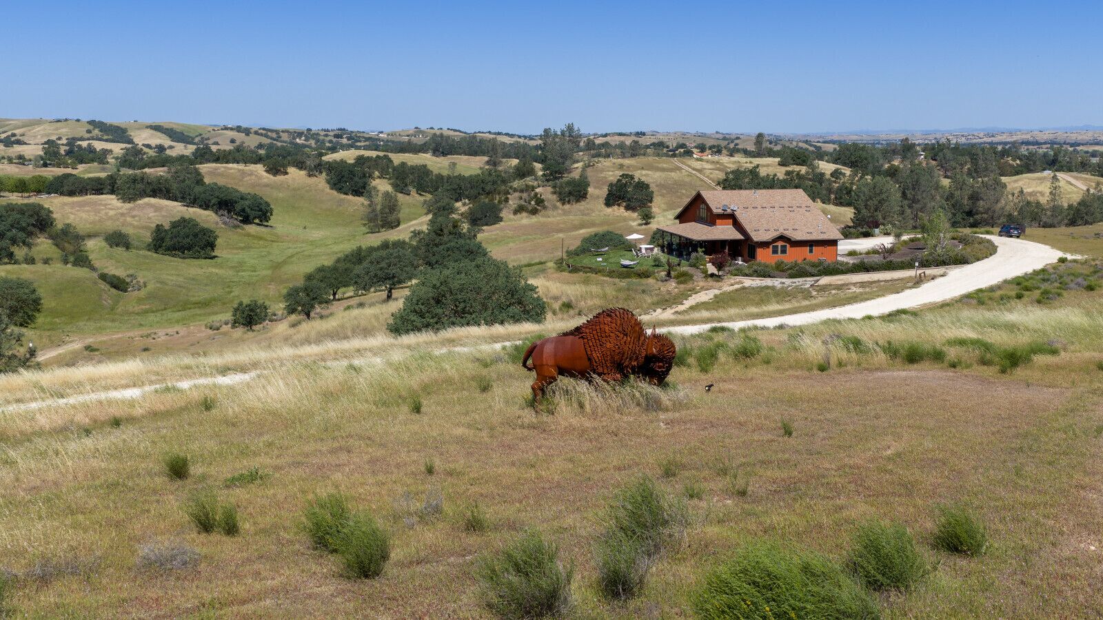 A rural landscape with a house, a dirt road, and a horse grazing.