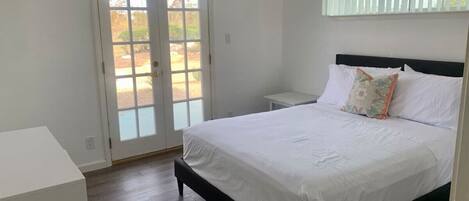 Un dormitorio con cama, mesita de noche, cómoda y una puerta corrediza de vidrio que da a un espacio exterior.