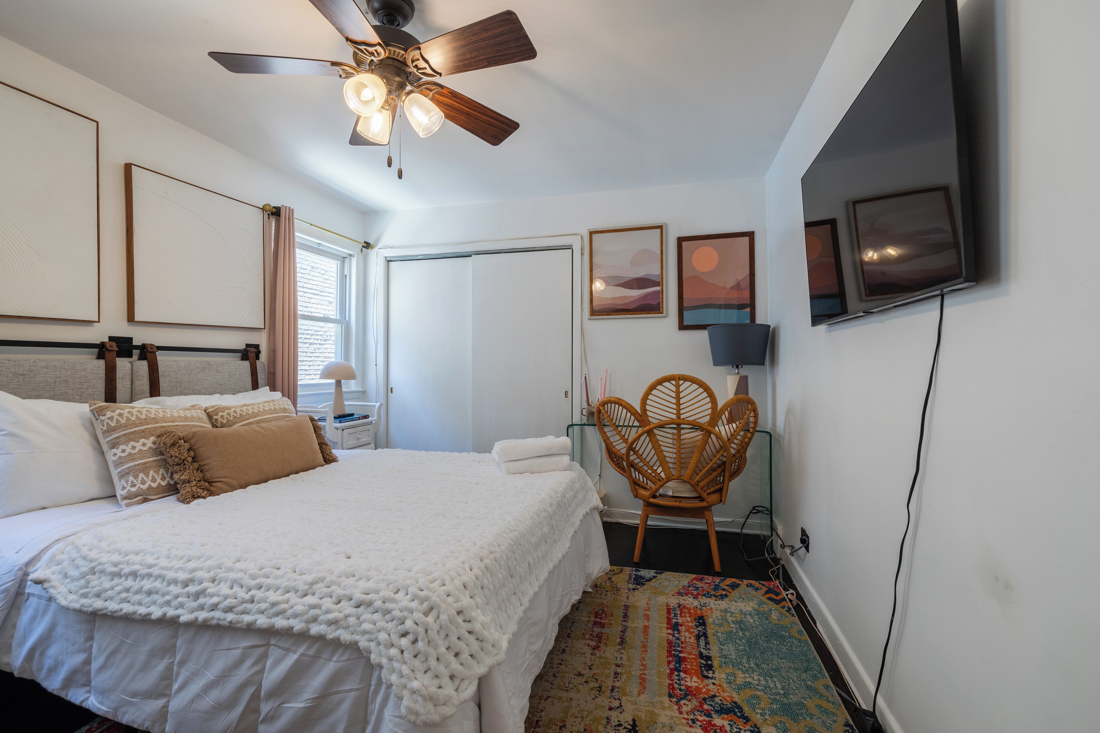 A bedroom with a bed, a ceiling fan, a TV mounted on the wall, and a chair.