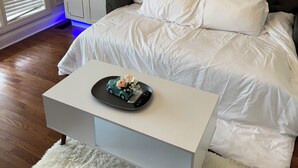 Une chambre à coucher avec un lit, des rideaux blancs, une armoire et une petite table sur laquelle est posé un objet décoratif.