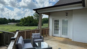 Une terrasse extérieure couverte, aménagée avec des meubles en osier et une table en verre, qui offre une vue sur une pelouse et une maison.