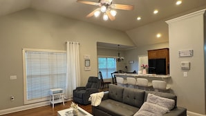 Un salon spacieux avec un canapé d’angle, une table basse blanche et un ventilateur de plafond.
