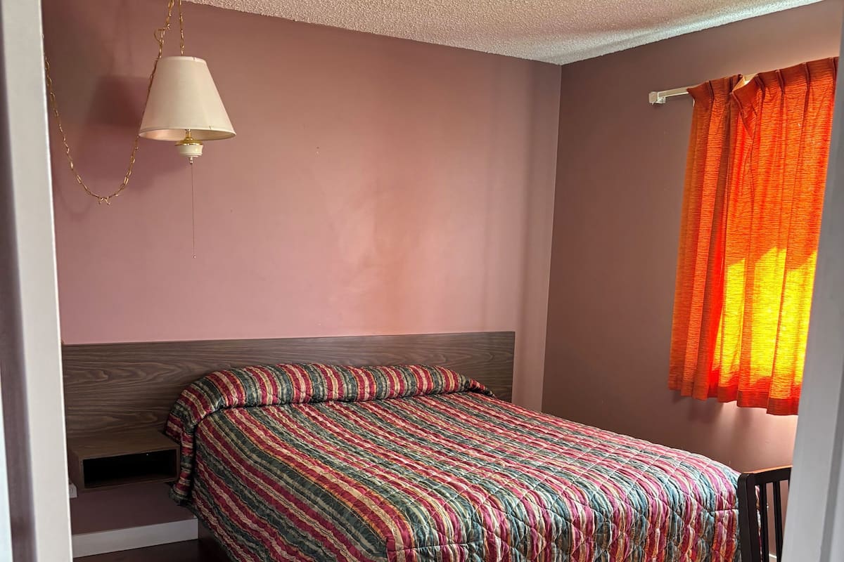 Una habitación con cama, escritorio, lámpara colgante y ventana con cortinas.