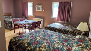 A room with two beds, a table with chairs, a lamp, and a window with curtains. - Lamplighter Viking Motel (Viking)