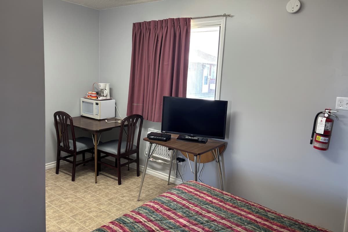 Una habitación con cama, televisión, microondas y una mesa con sillas.