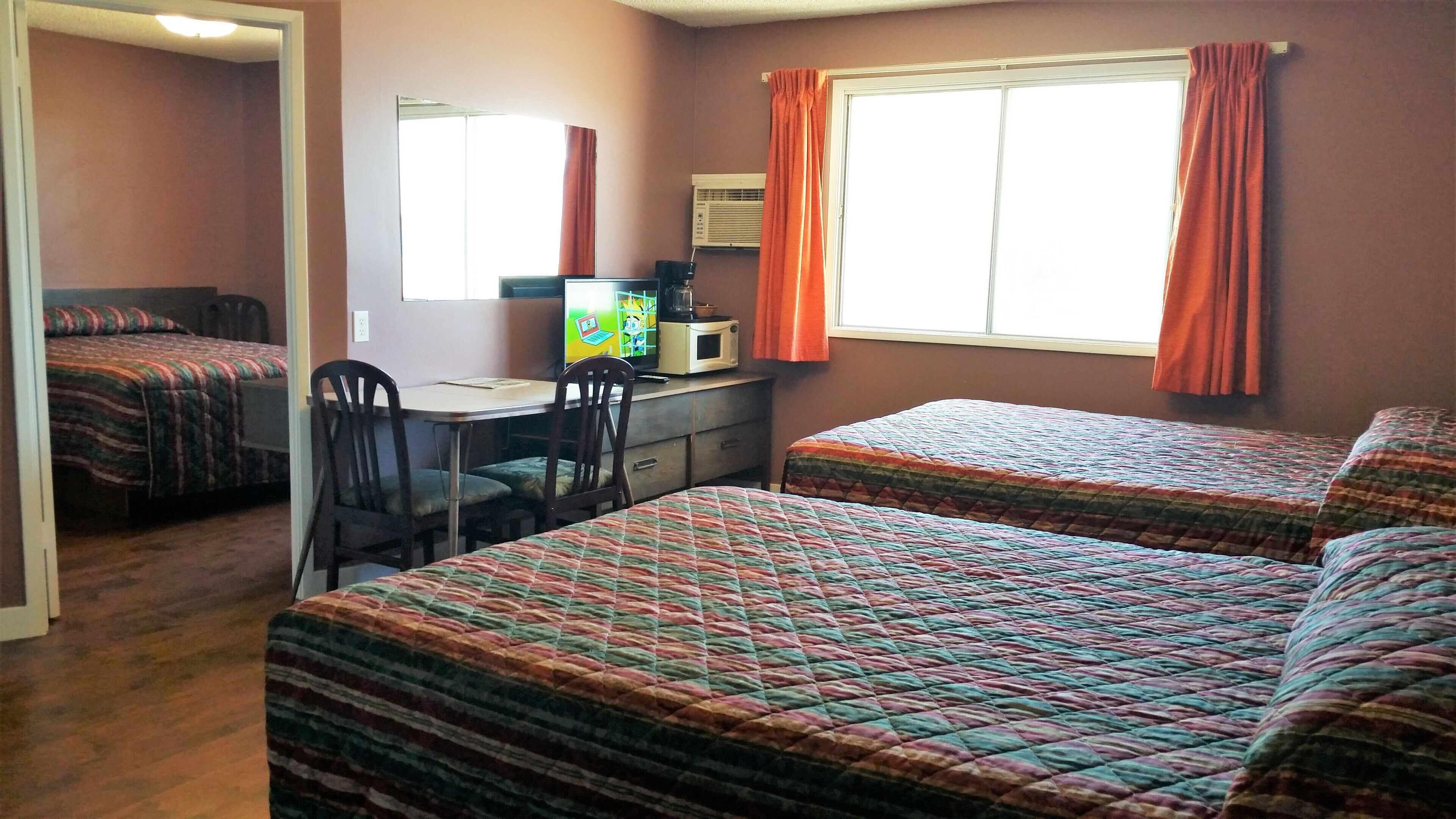 A room with two beds, a desk, and a chair. There is a window with curtains and an air conditioning unit on the wall.