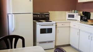 A compact kitchen with a refrigerator, stove, microwave, and a dining table with chairs. - Lamplighter Viking Motel (Viking)