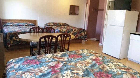 Habitación de motel con dos camas individuales, una pequeña mesa de comedor y un refrigerador.