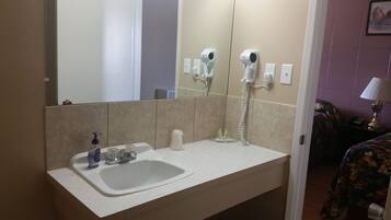 A bathroom with a sink, hand soap dispenser, and a hairdryer mounted on the wall.