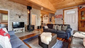 A cozy living room with a stone wall, a fireplace, a television, and a comfortable seating area. - Waterfront Cottage ~ Fireplace ~ Kawartha (Lakefield)
