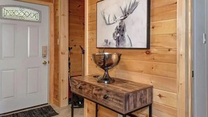 A wooden interior with a white door, a framed moose artwork, and a metal bowl on a wooden table. - Waterfront Cottage ~ Fireplace ~ Kawartha (Lakefield)