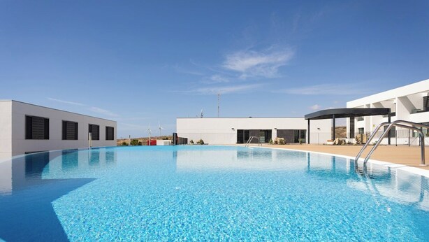 En modern byggnad med en swimmingpool, ett takförsett utomhusområde och en klar himmel.