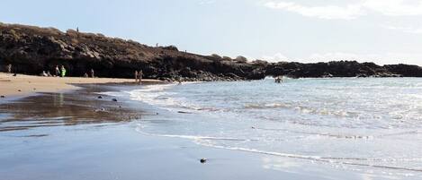 A beach with clear water, sandy shore, and rocky cliffs.