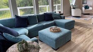 A modern living room with a sectional sofa, a round coffee table, and a view of a balcony with railings. - Dungeness Bay Hideaway (Sequim)