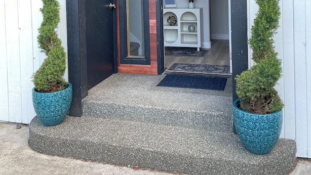 A modern entrance with a dark door, a white interior visible through the doorway, and two potted evergreen plants on either side. - Dungeness Bay Hideaway (Sequim)