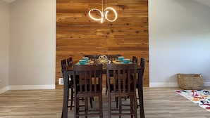 A dining area with a wooden wall, a round table, and chairs. - Dungeness Bay Hideaway (Sequim)
