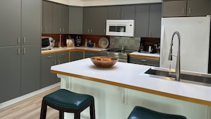 A modern kitchen with grey cabinets, a white island with stools, a skylight, and a built-in microwave. - Dungeness Bay Hideaway (Sequim)