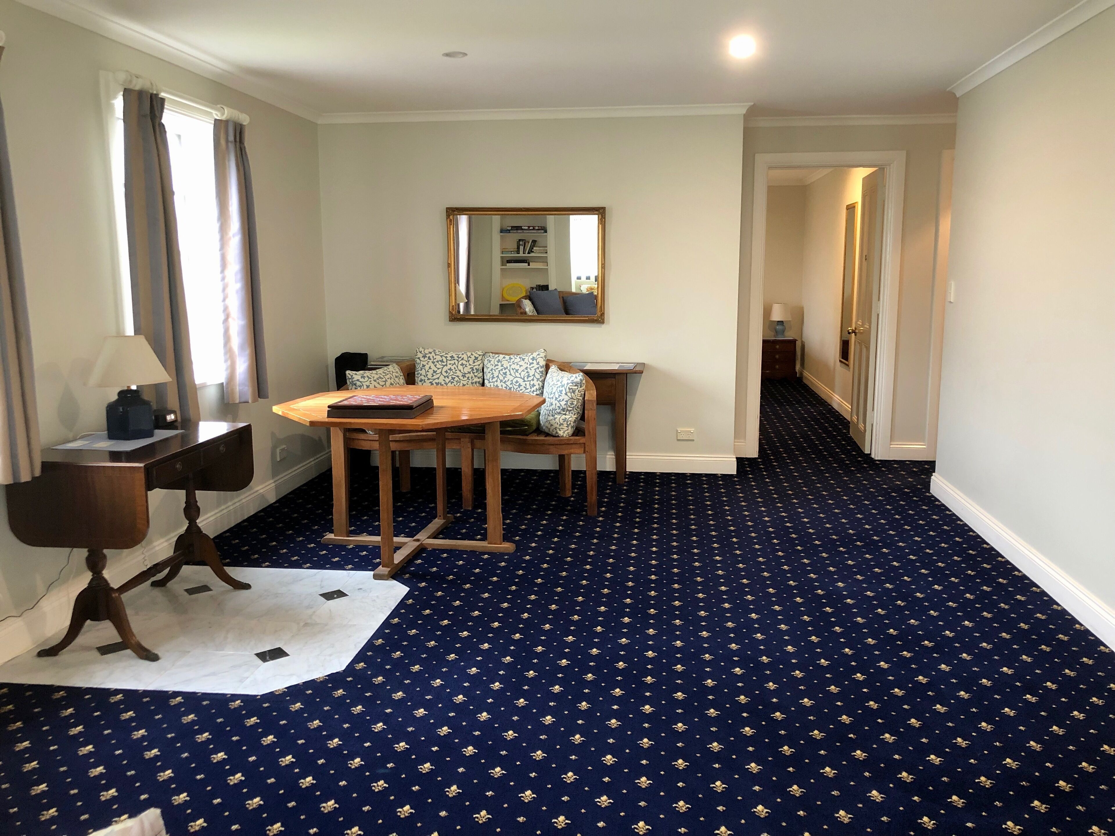 A hotel room with a dining table, a sofa, a mirror, and a patterned carpet.