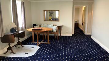 A hotel room with a dining table, a sofa, a mirror, and a patterned carpet.