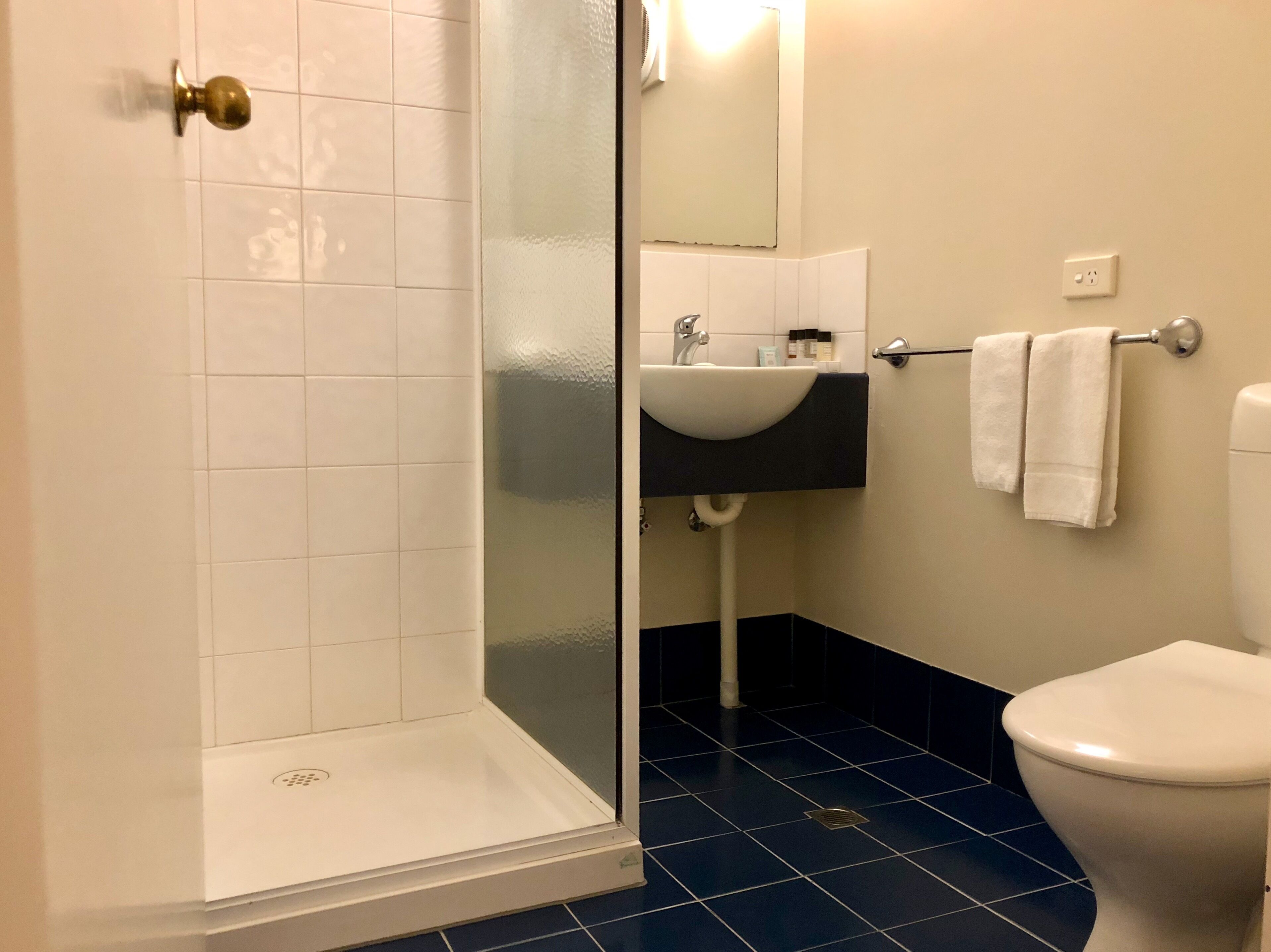 A bathroom with a glass shower enclosure, a white sink, a black countertop, and a white toilet.