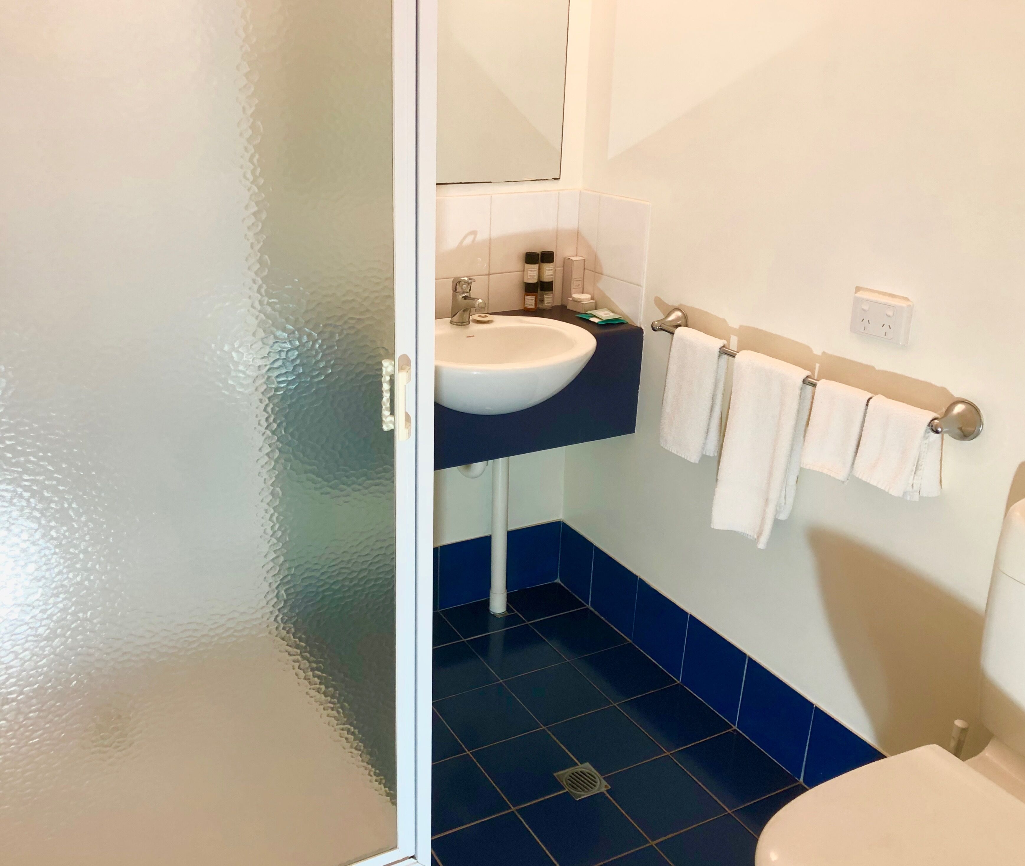 A bathroom with a white sink, blue-tiled floor, and a white toilet.